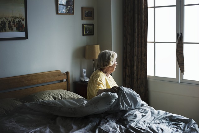 Stará žena sedí na posteli so sivými paplónmi.jpg